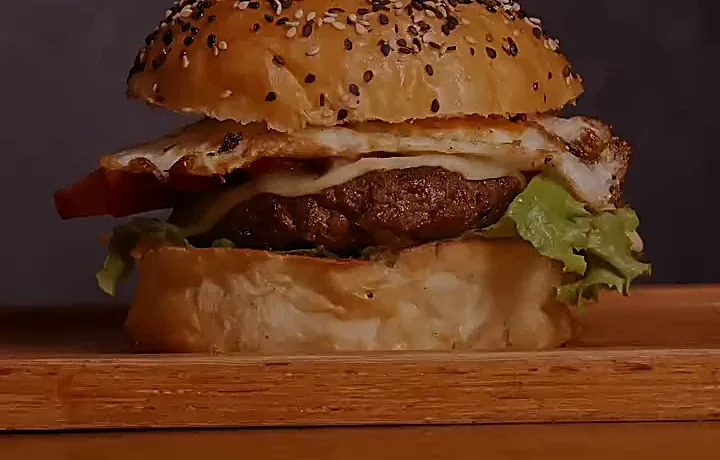 Hamburguesa con huevo frito y queso en pan con ajonjolí, sobre tabla de madera