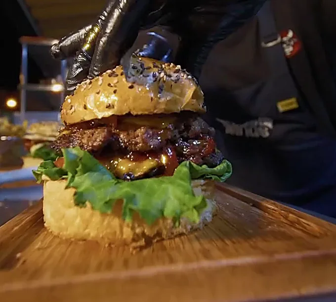 Cocinero con guante negro armando una Toro de Lidia con onion ring sobre tabla de madera